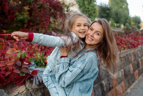Beautiful young family mom hugs her pretty daughter on a walk in the park in autumn - 写真・画像