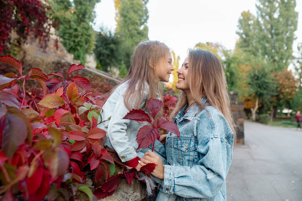 Beautiful young family mom hugs her pretty daughter on a walk in the park in autumn - Фото, зображення