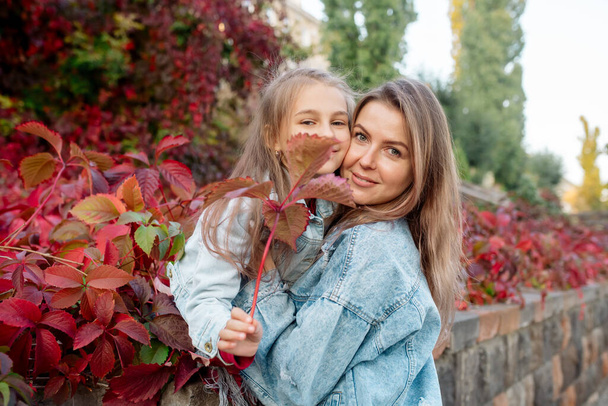 Beautiful young family mom hugs her pretty daughter on a walk in the park in autumn - Foto, afbeelding