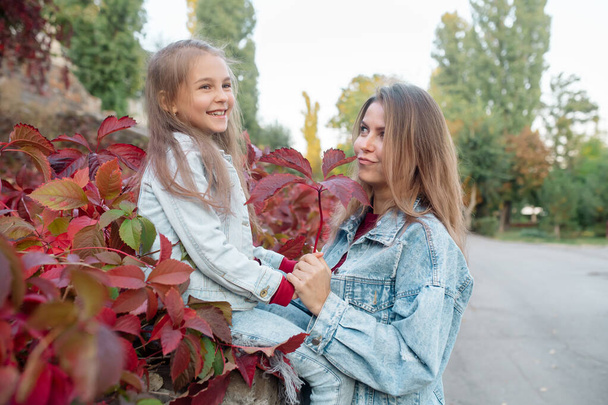 Beautiful young family mom hugs her pretty daughter on a walk in the park in autumn - Fotoğraf, Görsel