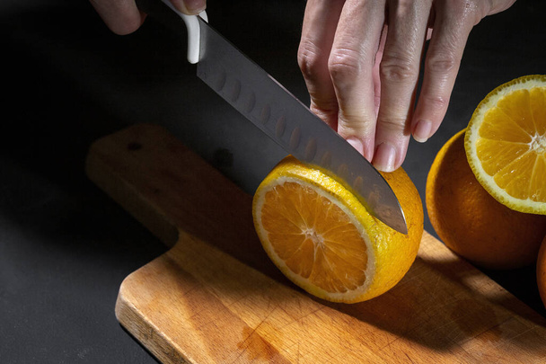 Unrecognizable woman hands cutting fresh healthy orange slices on wooden board - 写真・画像