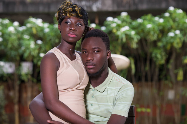 若いアフリカ人のカップルがカメラを見ながら椅子に座って. - 写真・画像