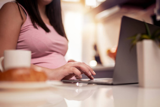 Беременная женщина работает из домашнего офиса и завтракает. - Фото, изображение