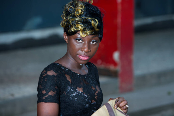 Lähikuva kasvot hymyilevä Afrikkalainen nainen istuu kädessään piilotettu pussi ja katsot kameraa. - Valokuva, kuva