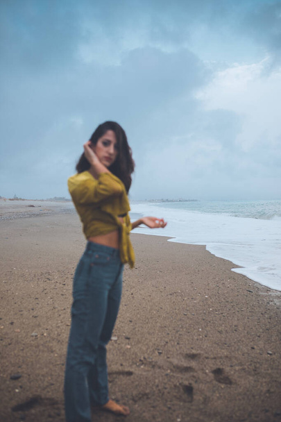 Young woman posing at beach opposite ocean - 写真・画像