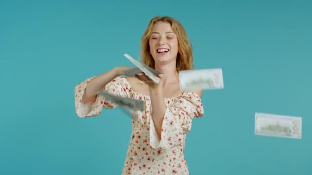 Pretty woman with happy face scatters, waste money. Cute girl with blonde hair overspend US currency. Lady is flush with dollars on blue studio background . - Filmmaterial, Video
