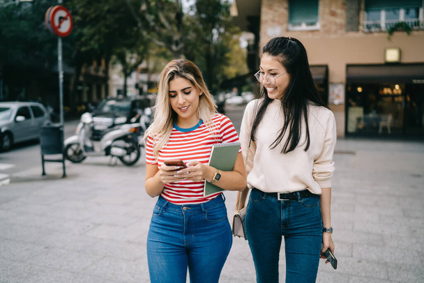 Multiracial hipster girls enjoying mobility chatting and messaging during city sightseeing on vacations, charming female bloggers using smartphone for making online booking and travel ticketing - Fotoğraf, Görsel