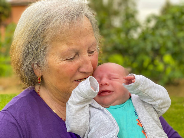 Γιαγιά αγκαλιάζει νεογέννητο ανιψιό της υπαίθρια. - Φωτογραφία, εικόνα