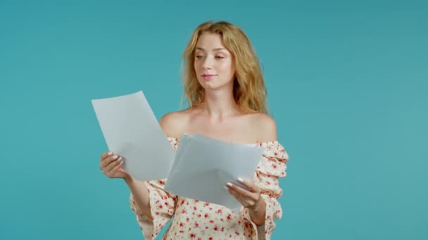 Pretty girl checks documents, utility bills. Smiling woman standing on blue background. She is satisfied. - Video, Çekim