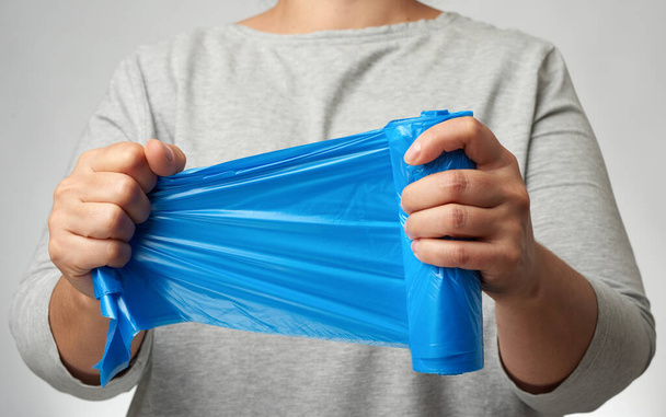 mujer sosteniendo un rollo de bolsas de basura azul en su mano, fondo gris - Foto, Imagen