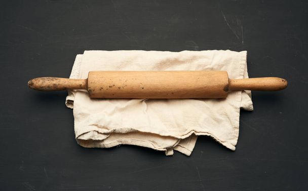rolo de madeira pino mentira em um guardanapo de linho cinza, mesa preta, vista superior - Foto, Imagem