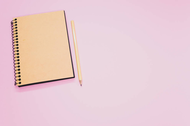 A high angle shot of a notebook and a pencil on a pink surface - Foto, immagini