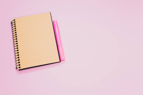 A high angle shot of a notebook and a pink marker on a pink surface - Fotoğraf, Görsel