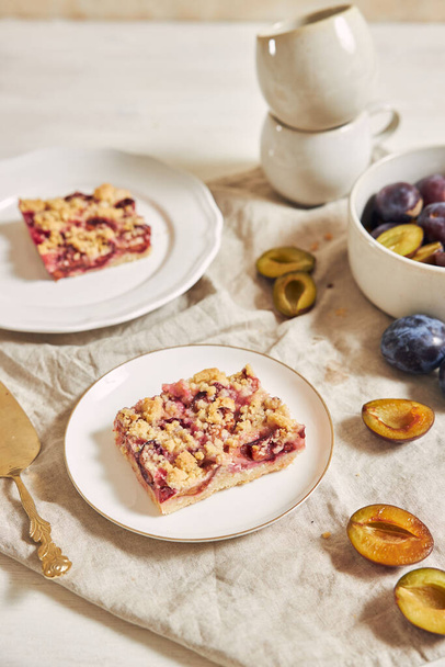 Delicious homemade plum cake with crumbles on plates on a white table - Fotó, kép
