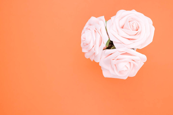 A top view of three artificial light pink roses placed in a pot isolated on an orange background - Фото, изображение
