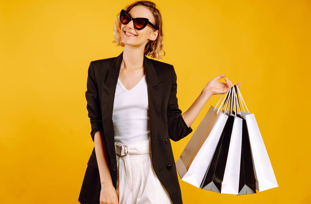Beautiful woman after shopping posing on yellow background. Young woman with black and white shopping bags. Purchases, black friday, discounts, sale concept. - Фото, зображення