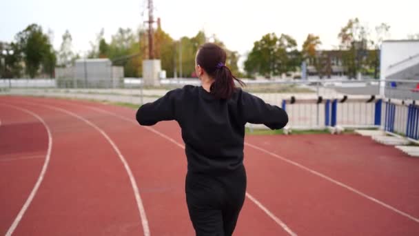 Active woman at stadium. Young fit female in sportswear and protective mask for coronavirus prevention running on red track during outdoor workout at stadium. - Footage, Video