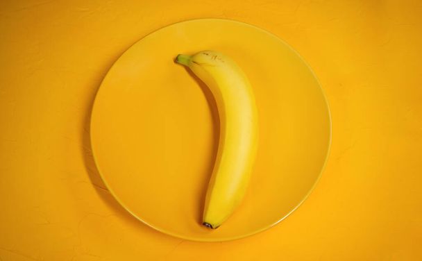 Banana on a yellow plate. Yellow banana on a yellow textured background. Concept: fruit and healthy food. - Photo, image