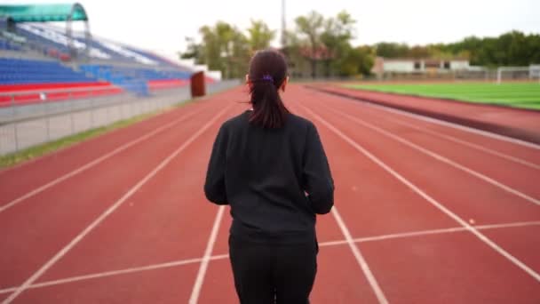 Active woman at stadium. Young fit female in sportswear and protective mask for coronavirus prevention running on red track during outdoor workout at stadium. - Video, Çekim