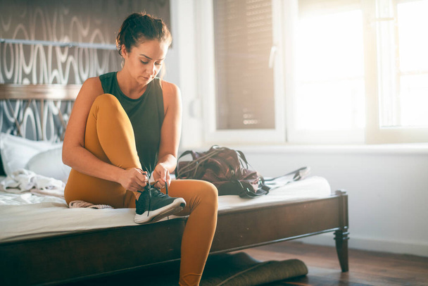 nainen urheilullinen vaatteet sitominen nauhat istuu sängyllä - Valokuva, kuva