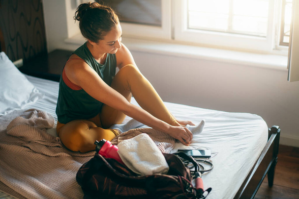 γυναίκα σε αθλητικά ρούχα βάζοντας κάλτσα στο κρεβάτι πριν από την κατάρτιση - Φωτογραφία, εικόνα