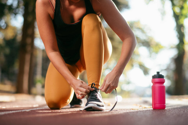cropped shot of woman tying laces on trainer shoe with water bottle on ground - Foto, afbeelding