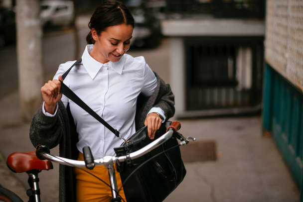souriant jeune femme regardant sac debout à vélo - Photo, image