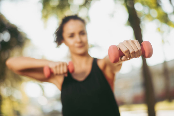 woman in sportive clothes holding dumbbells outdoors - Photo, Image