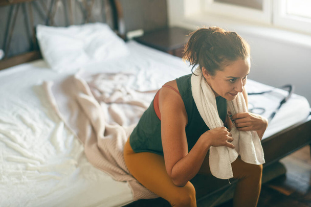 femme en vêtements de sport avec serviette assise sur le lit - Photo, image