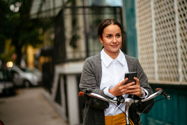 Bisikletli ve akıllı telefonlu gülümseyen bir kadın.  - Fotoğraf, Görsel