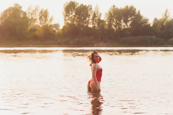 Beautiful young woman in red swimsuit posing near river. Summer lifestyle. - 写真・画像