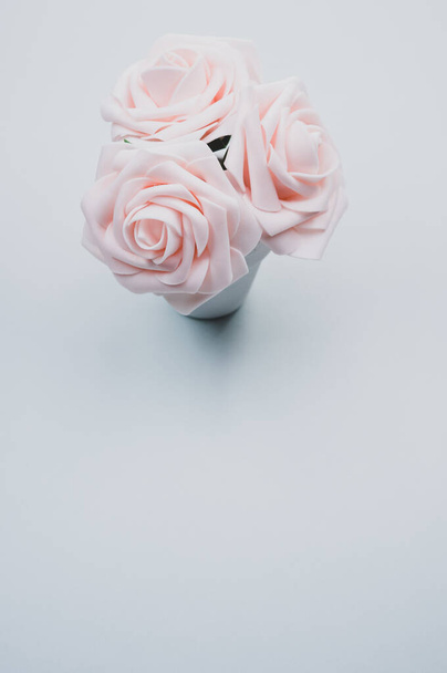 A top view closeup of three artificial light pink roses placed in a pot isolated on a blue background - Photo, image