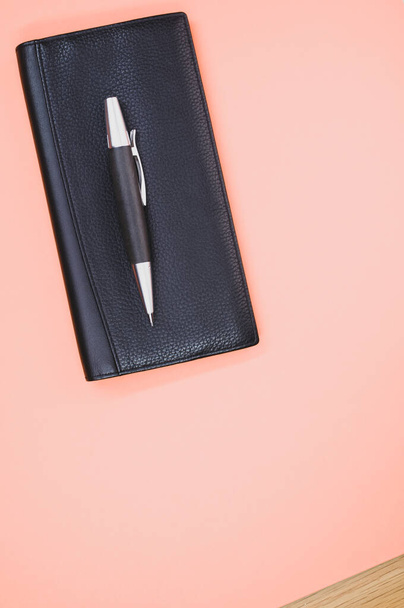 A closeup of a rollerball pen on a small wallet isolated on a light pink background - Foto, Bild