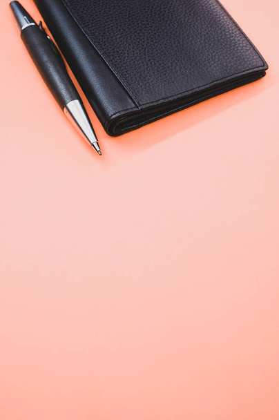 A rollerball pen next to a small leather wallet isolated on a light pink background - Foto, Bild