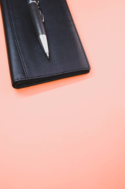 A closeup of a rollerball pen on a small wallet isolated on a light pink background - Fotó, kép