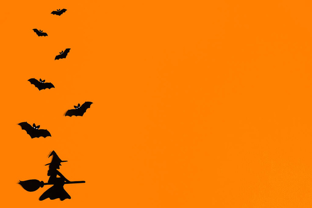 Silhouettes of a flock of bats and a witch flying on a broom made of black paper on an orange background. Halloween greeting template with copy space. Flat lay for your design. ready-made template - Fotografie, Obrázek