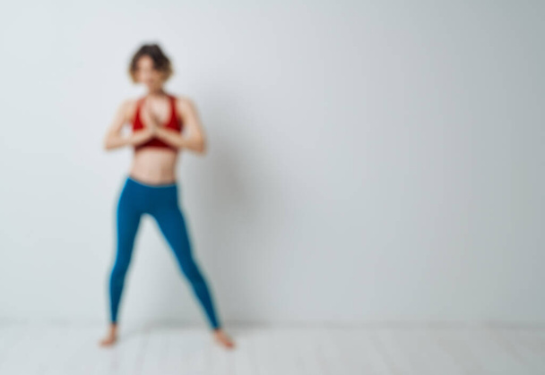 woman doing yoga in a bright room and blue leggings red tank top - Foto, Imagen