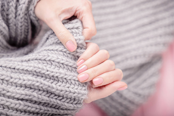 Female hands holding large gray woolen scarf. Manicure with pink color nail polish, shiny design. Top view, copy space - Foto, afbeelding