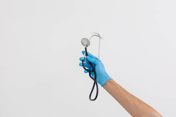 Blanke mannelijke hand, medische handschoenen dragend, stethoscoop vasthoudend, witte achtergrond - Foto, afbeelding
