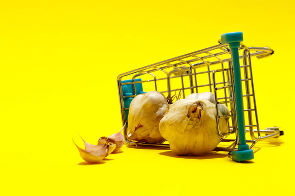 Garlic in a supermarket cart on yellow background. online shopping concept - Photo, Image