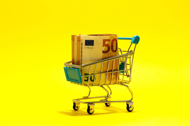 Billets en euros dans un panier de supermarché sur fond jaune. concept d'achat en ligne.Petit budget concept - Photo, image