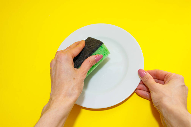 Female hand holds a plate and sponges it on yellow background. Washing dishes. Top view.Flat lay - Photo, Image