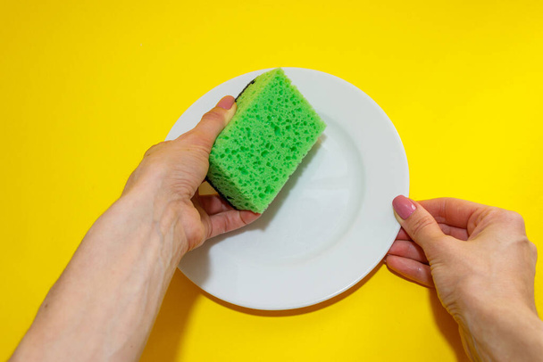 Female hand holds a plate and sponges it on yellow background. Washing dishes. Top view.Flat lay - Φωτογραφία, εικόνα