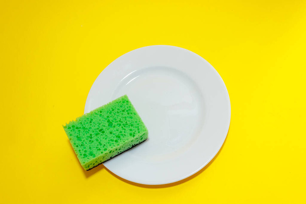 Esponja de limpieza sobre un plato blanco sobre un fondo amarillo.Puesta plana - Foto, imagen