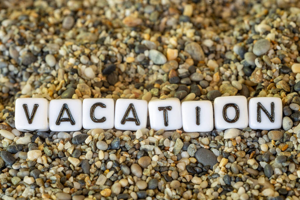 海辺の砂の石に描かれた手紙の静物の休暇先の都市の名前と休暇碑文のテキスト - 写真・画像