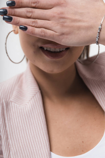 Schöne lachende junge Frau, die ihre Augen mit den Händen vor hellem Studiohintergrund bedeckt - Foto, Bild