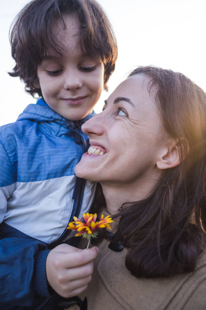 Un enfant donne une fleur à sa mère, un garçon marche avec sa mère, une femme renifle une fleur, un portrait d'une femme souriante. - Photo, image