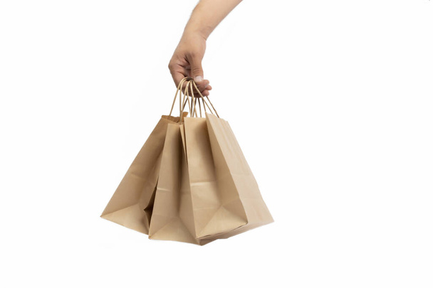 Mano con sacchetti di carta su sfondo bianco. Stagione dello shopping come regalo per le vacanze. consegna di prodotti in imballaggi ecologici - Foto, immagini