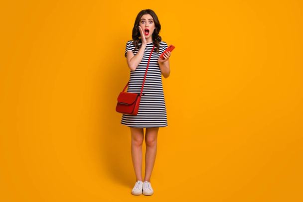 Full length photo of crazy wavy lady chatting friends hold telephone read good news blogger wear casual striped short dress clutch shoes isolated yellow color background - Photo, image