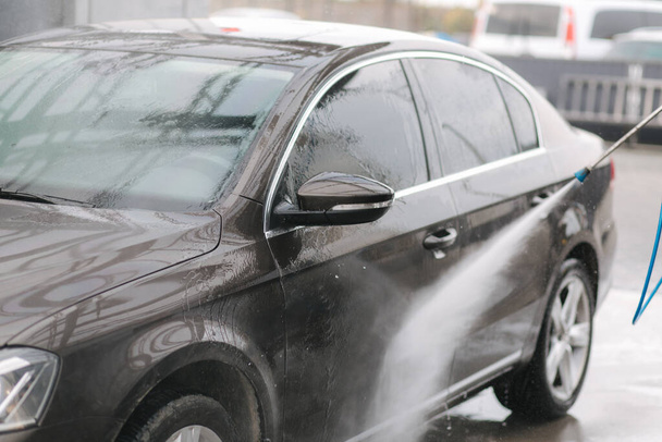 洗車場だ。高圧水を使って車を掃除する。男は車を屋外で洗っている。閉鎖 - 写真・画像